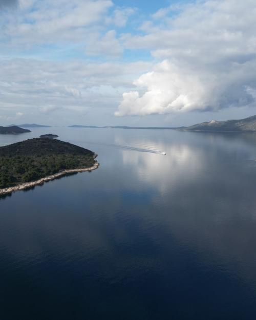 Serene aerial shot of Mali Iž island reflecting on the Adriatic Sea with a cloudy sky.
