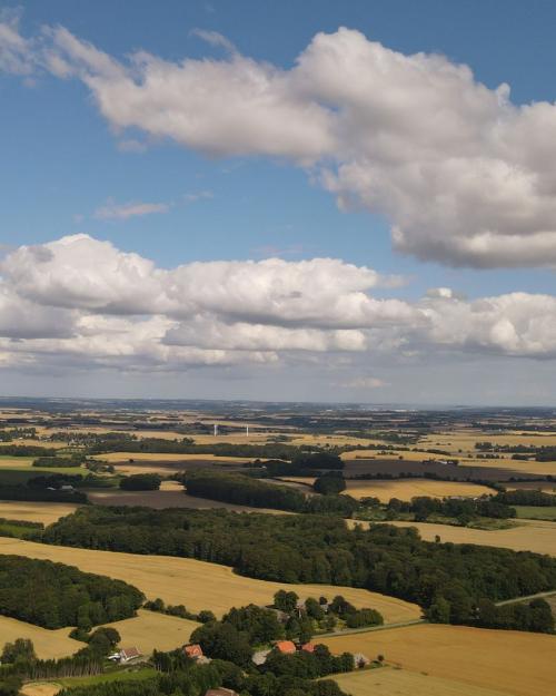 Aerial view of lush farmland in Rask Mølle, Denmark, with a vibrant sky and rolling fields.