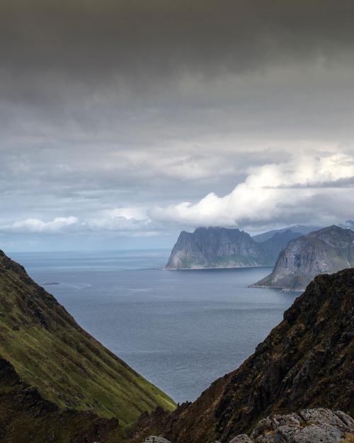 A stunning view of the Lofoten fjord surrounded by rocky mountains and a dramatic cloudy sky.