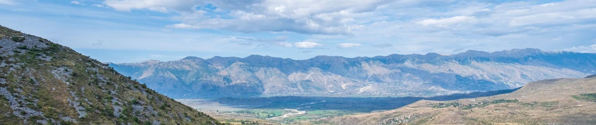 Breathtaking view of the Albanian countryside with mountains and lush valleys under a bright blue sky.