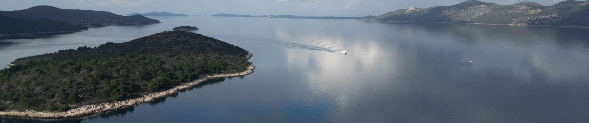 Serene aerial shot of Mali Iž island reflecting on the Adriatic Sea with a cloudy sky.