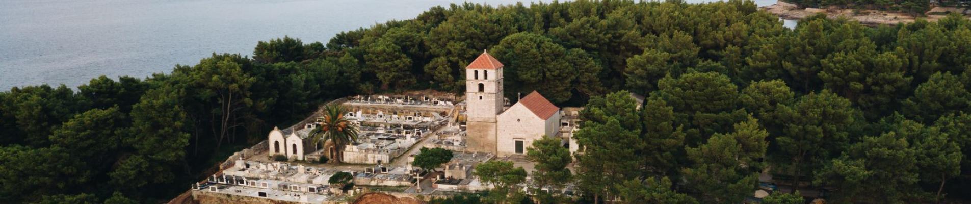A serene aerial view of a historic church nestled amid lush greenery along the scenic Jelsa coastline in Croatia.