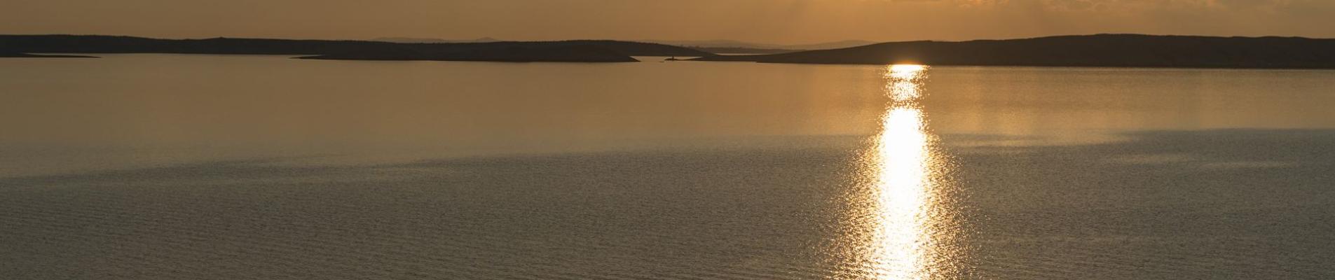 Tranquil scene of a lone boat during a golden sunset over the Adriatic Sea in Pag, Croatia.