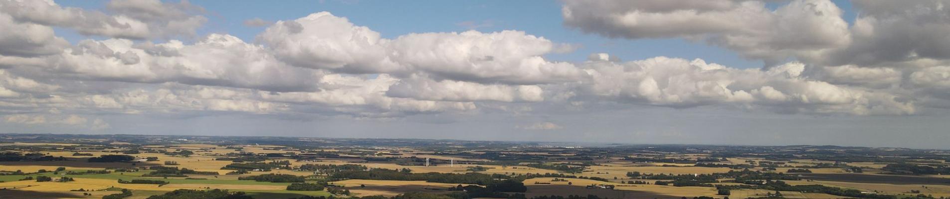 Aerial view of lush farmland in Rask Mølle, Denmark, with a vibrant sky and rolling fields.