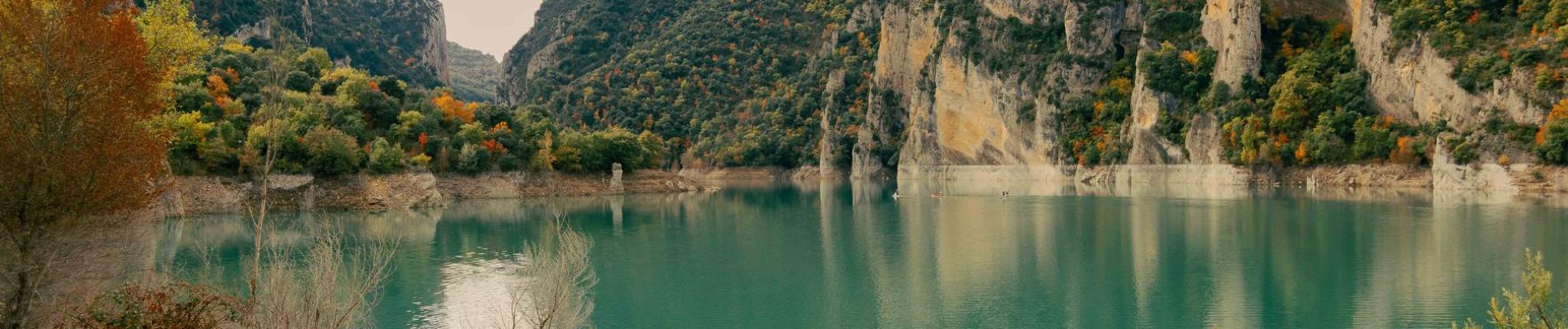Explore serene turquoise waters amid autumn foliage and rocky mountains in Spain.