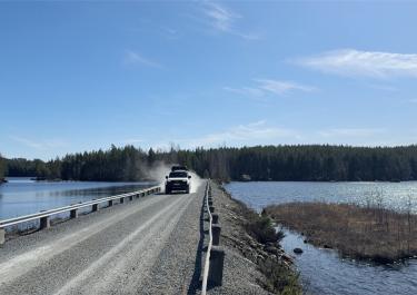 Auto fährt auf einem Schotterweg; link und rechts des Weges ist Wasser 