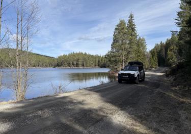 Weißes Offroadauto fährt auf einer breiten Schotterstraße an einem See entlang