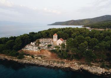 A serene aerial view of a historic church nestled amid lush greenery along the scenic Jelsa coastline in Croatia.