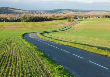 Serene countryside road through green fields in Gommecourt, IDF, France.