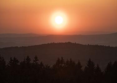 Stunning sunset over Bavarian forest and hills, with vibrant twilight colors.