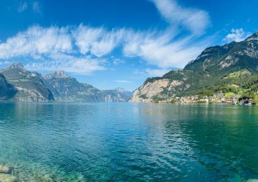 Stunning panoramic view of a lake with mountain backdrop under a bright sky in Flüelen, Switzerland.